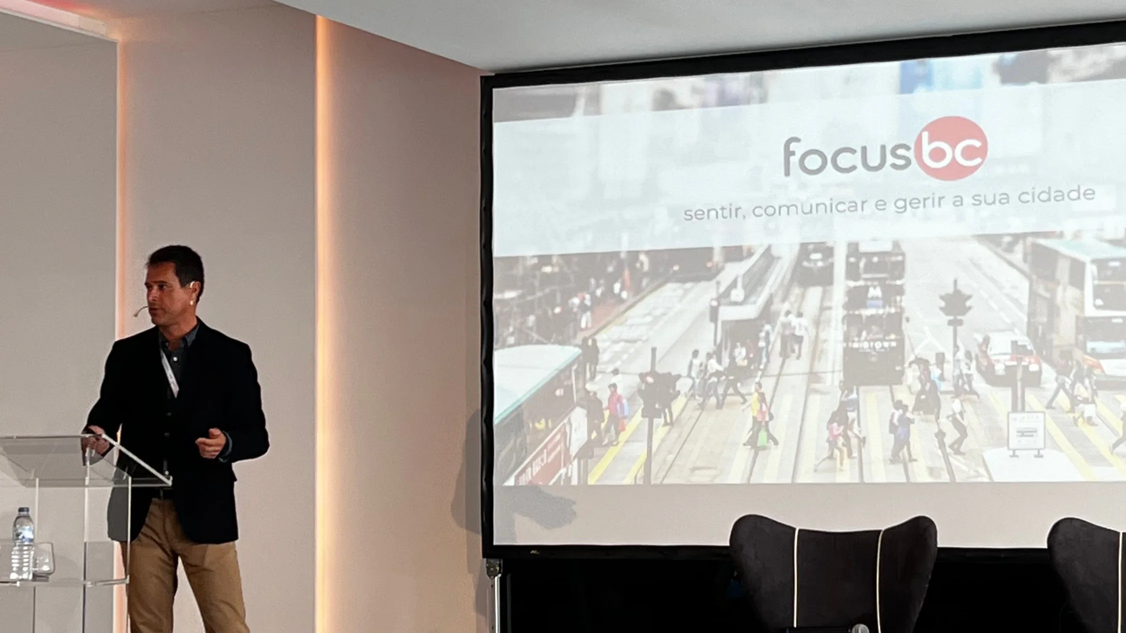 Speaker presenting Focus BC’s urban platform on stage, with a slide reading “focusbc – sentir, comunicar e gerir a sua cidade” projected behind him.