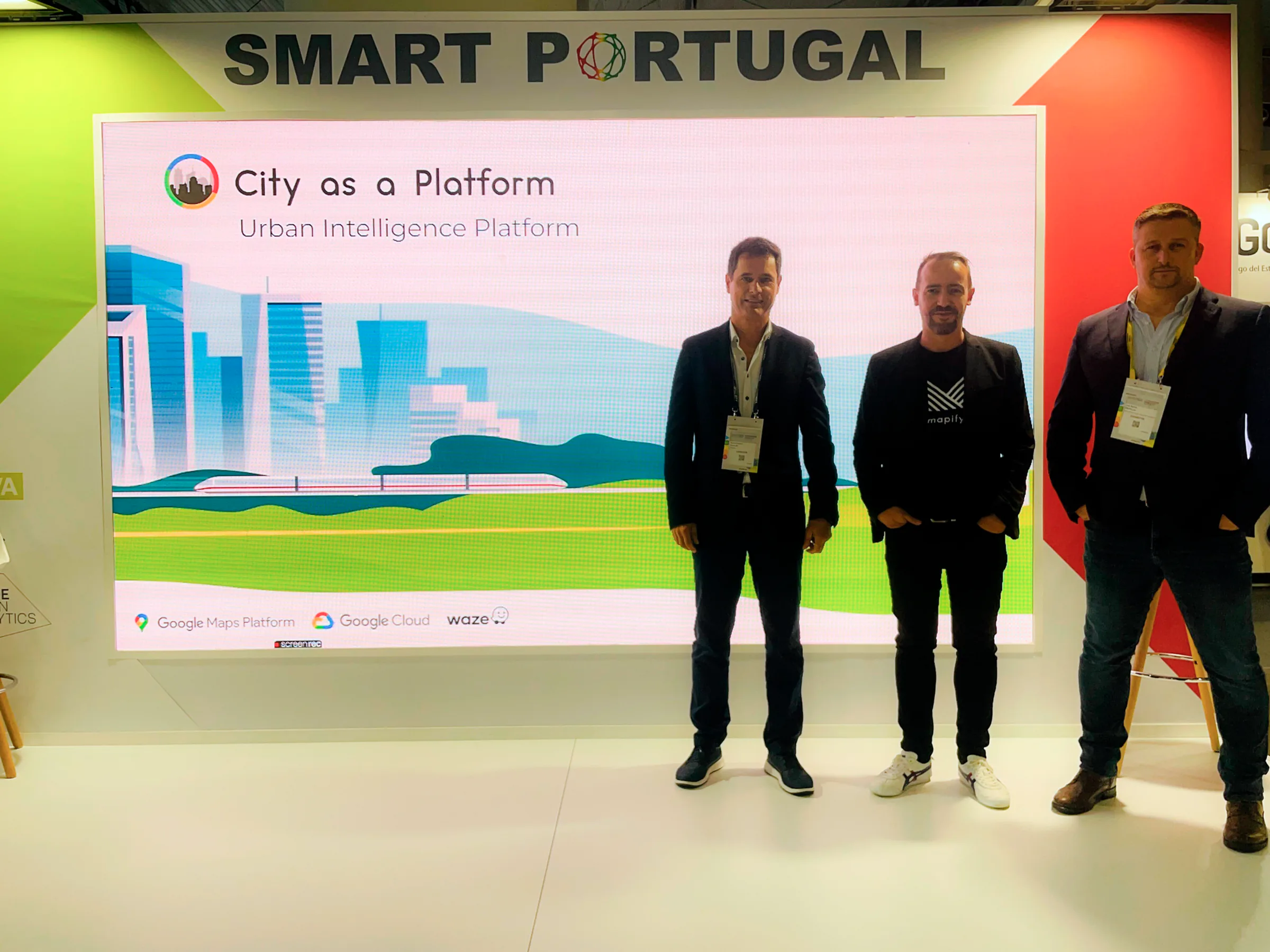 Vasco, Sandro and João standing in front of a large “Smart Portugal” exhibition display showcasing the “City as a Platform – Urban Intelligence Platform” solution.