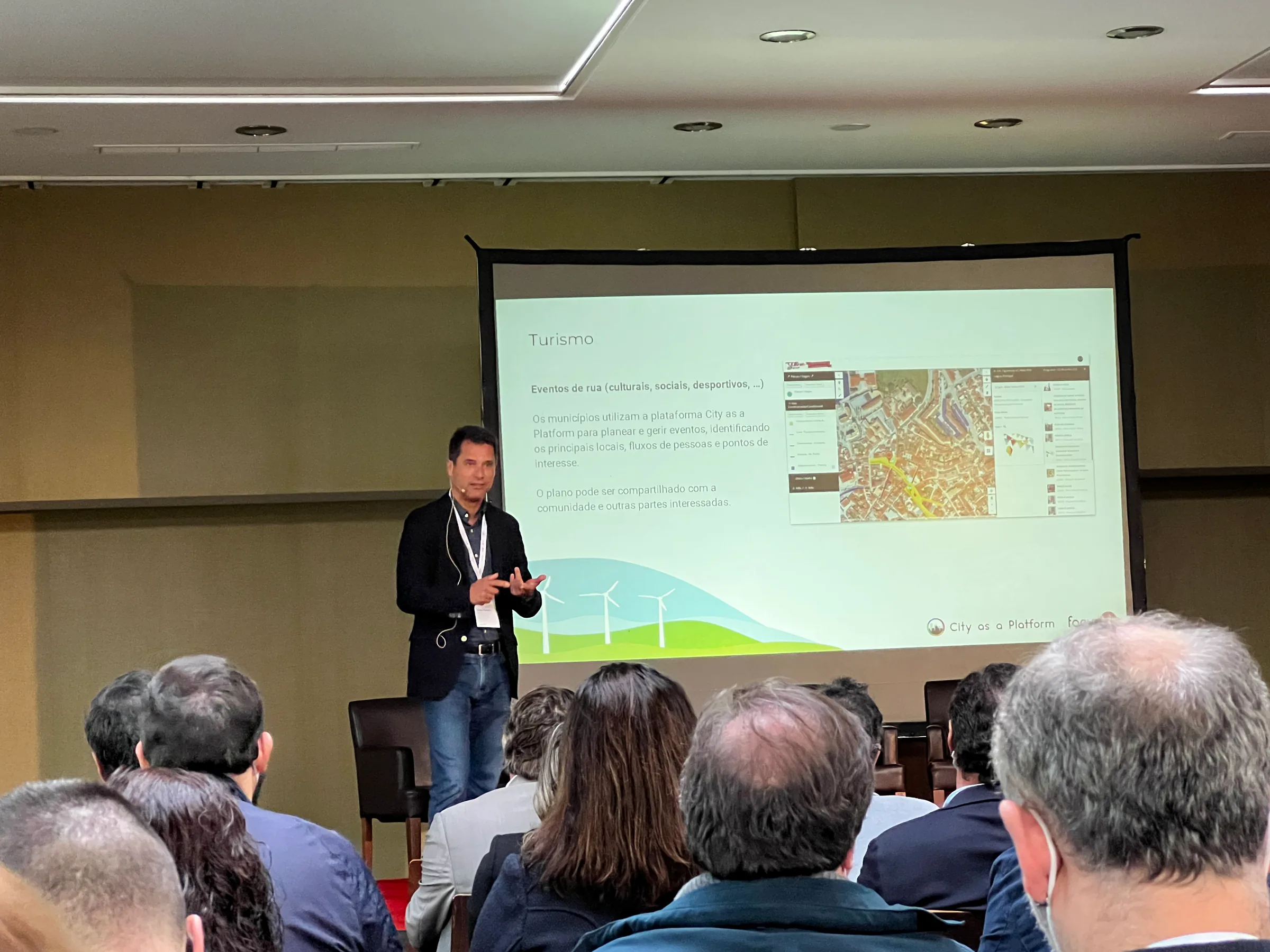 Speaker presenting a “Tourism” slide about City as a Platform to an audience seated in a conference room.