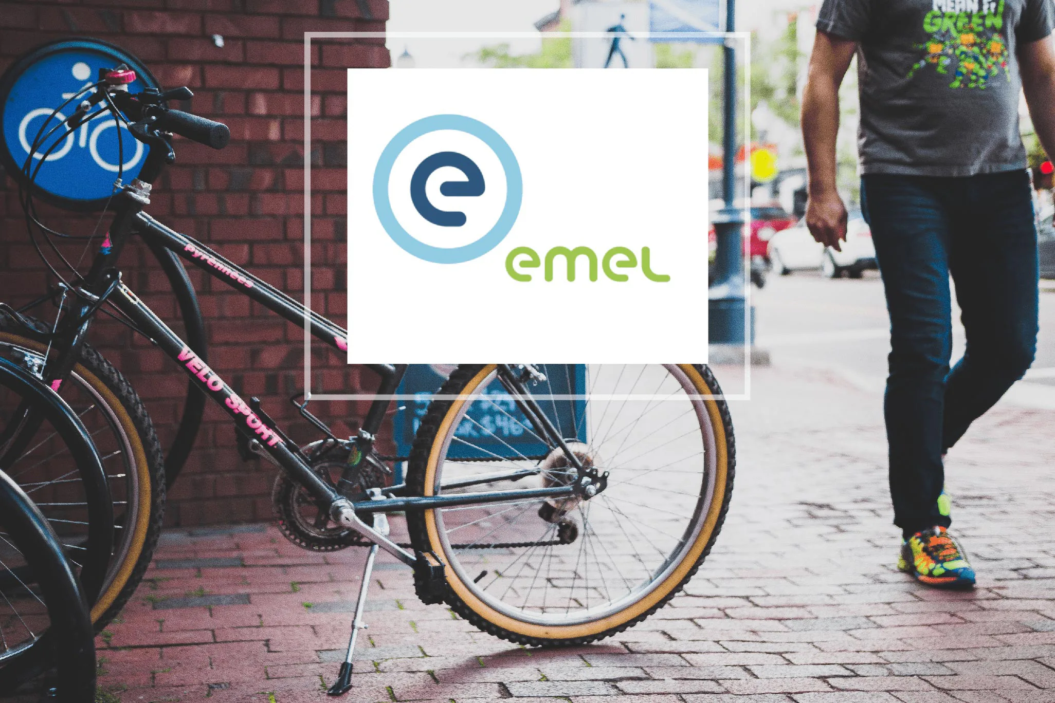 EMEL logo overlaid on a city street scene featuring a parked bicycle and a pedestrian walking on a cobblestone sidewalk.